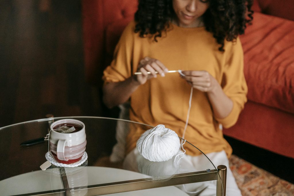 Woman sitting on floor crocheting drinking a cup of tea